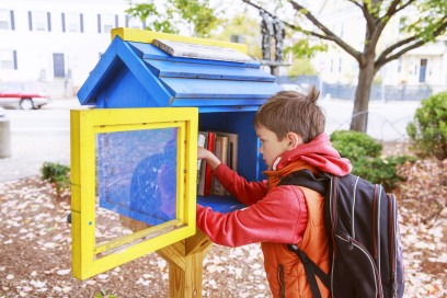 boy takes the free books on the street. little free street library. schoolboy choosing a book to borrow
